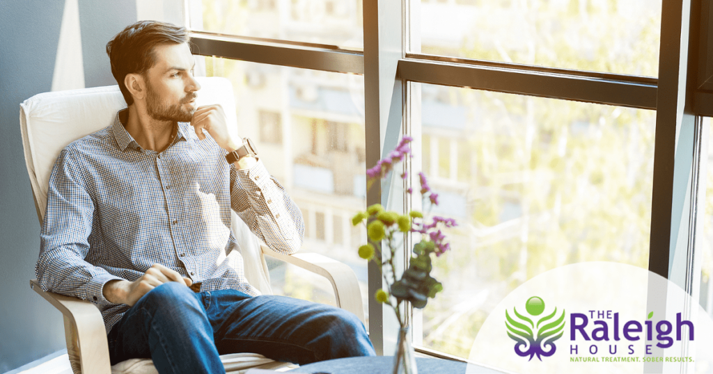 A young man sits in a chair, looking out the window.