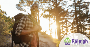A woman in the middle of a hike sits on a log to take a rest with a big smile on her face.