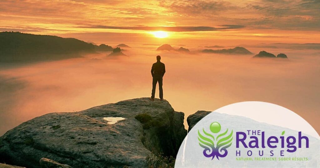 A hiker standing on the top of a mountain looks out at an autumn sunset.
