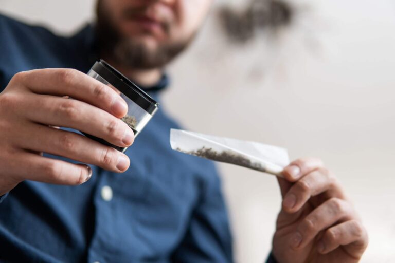 A man rolling a marijuana joint at home while struggling with marijuana abuse.
