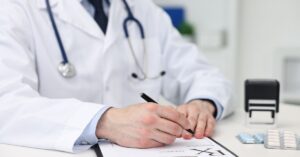 Doctor writing prescription at white table in clinic