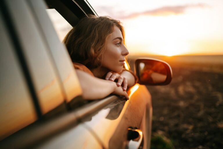 Happy woman outstretches her arms while sticking out the car window.