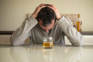 Man holding head over glass of alcohol